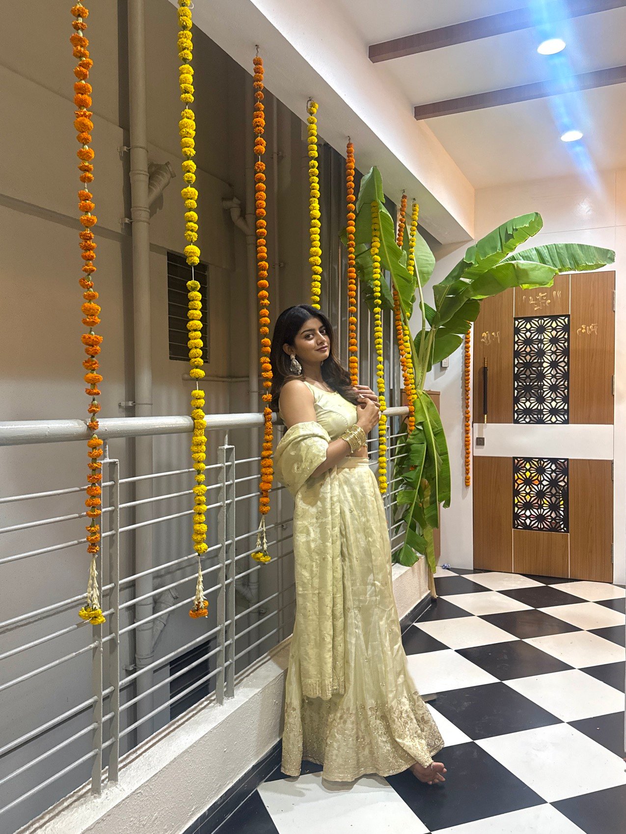 Festive golden lehenga shoot beside hanging marigold garlands